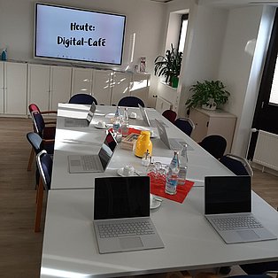 Besprechungsraum des Paritätischen Oberhausen. Gedeckter Tisch u.a. mit Kaffeetassen und Tablets. An der Wand hängt ein Bildschirm.