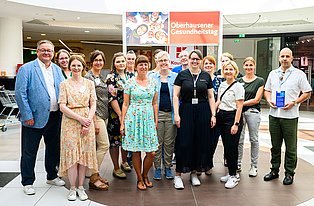 Buntes Bild, zu sehen sind insgesamt 16 Personen, u.a. der Bürgermeister Herr Nakot und die Mitarbeiterin der Selbsthilfe-Kontaktstelle OB