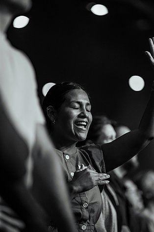 Frau mit geschlossenen Augen und geöffnetem Mund wie beim Singen, vor dunklem Hintergrund mit sichtbaren Lichteffekten ganz versunken