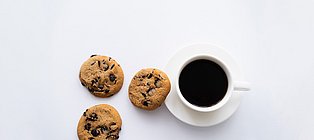 3 mit Schokolade gefüllte Plätzchen neben einer mit schwarzem Kaffee gefüllte Tasse