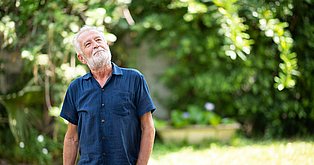 vor dem grünen waldigen Hintergrund steht ein Mann lächelnd mit Blick zu den Baumspitzen
