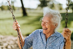 ältere Frau sitzt lachend auf einer Schaukel