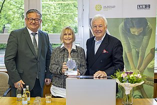 Foto mit drei Menschen die nebeneinander stehen und in die Kamera lächeln. Zu sehen sind v.l.n.r. Werner Nakot, Silvia Prochnau und Prof. D 