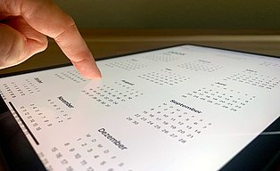 Bild mit Kalenderblatt und einem Finger, der auf ein Datum zeigt